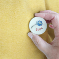 a ceramic brooch with a simple blue flower and the word love in red