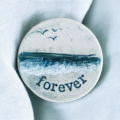 small handmade ceramic brooch with a sea scene and the word forever